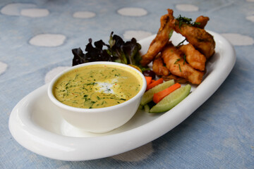 Coconut milk curry and battered fish fillet in a plate decorated with fruits and vegetables.
