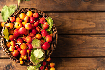 many small apples are lying in a wicker brown basket on a wooden table
