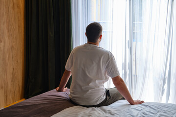 The man stretches after getting out of bed and looking out the window. Morning rituals for a...