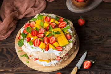 Pavlova with strawberries, mango and coconut cream. Cakes made of cane sugar. Tropical cake. Exotic dessert with mint. Strawberries on a wooden table. New Zealand food