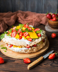 Pavlova with strawberries, mango and coconut cream. Cakes made of cane sugar. Tropical cake. Exotic dessert with mint. Strawberries on a wooden table. New Zealand food