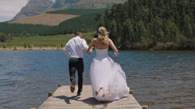 married couple jumping off jetty in lake bride and groom celebrating honeymoon sharing romantic wedding day