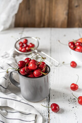 Sweet cherries in grey rustic cup, bawl and sieve on the white wooden background with napkin