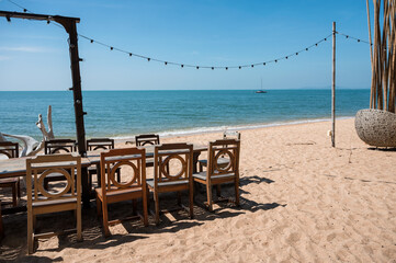 Celebration venue with wooden long table, chair, light bulb hanging and plant decoration in retro style on the beach