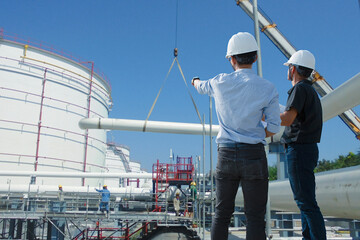 Two engineers work at a crude oil depot construction site. They are checking the progress of the...