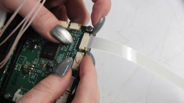 Woman with silver nails plugs flexible flat cable to chip assembling detail for refrigerator at workplace extreme close view