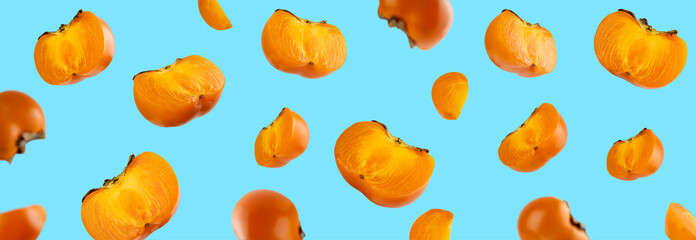Colorful floating orange fresh fruit whole and sliced organic persimmon with leaves on a blue background. Healthy eating and food concept. Levitations food. Creative layout for Design element
