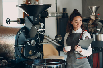 Coffee roaster machine and barista woman with tablet write pen at coffee roasting process.