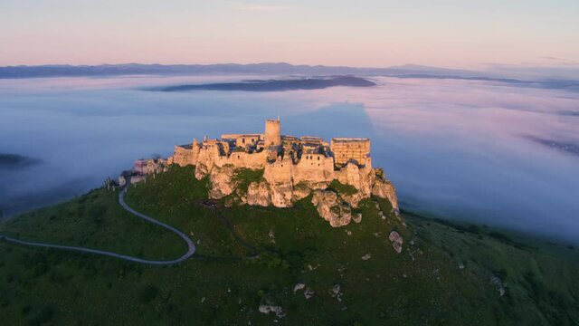 Aerial view of Spis Castle, standing above clouds, lit by morning sun, with shadow of the castle projection on fog below.  UNESCO listed, Slovakia.