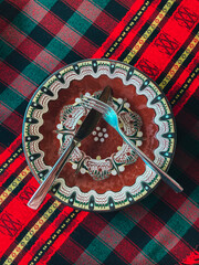 Traditional Bulgarian decorated ceramic plate on a red cloth, restaurant table. Fork and knife crossed in empty plate. - 454377774