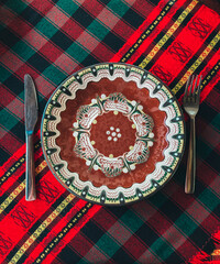 Traditional Bulgarian decorated ceramic empty plate on a red cloth, restaurant table. Fork and knife. - 454377796