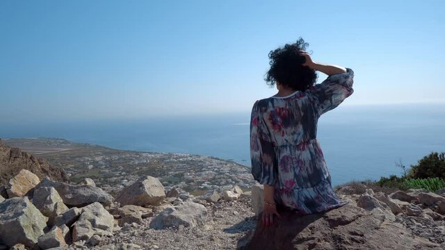 Young elegant woman enjoy view down the Ancient Thera mountain looking out over the sea and Kamari airport of Santorini Greece