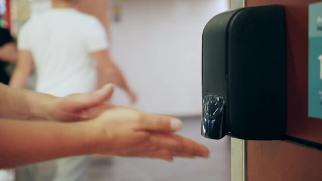 Close-up of hands using alcohol sanitizer sanitiser gel in public space. Cleaning, washing hand using automatic sanitizer dispenser concept.Travel safety measures concept.