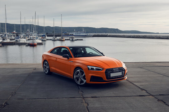 Samara, Russia - 09.05.2020: Orange AUDI A5 S line. A modern sports car is parked on the pier against the background of ships and yachts. Travel concept. Mountain view