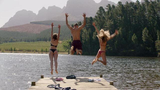 friends undressing jumping off jetty in lake at sunset having fun splashing in water enjoying freedom sharing summer vacation adventure