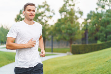 Young sports athlete man in white t-shirt run in the morning in modern park.