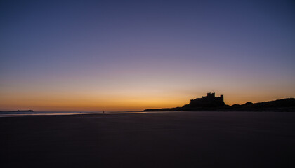 The iconic Bamburgh Castle in Northumberland at sunrise, with the nearby beach deserted.
