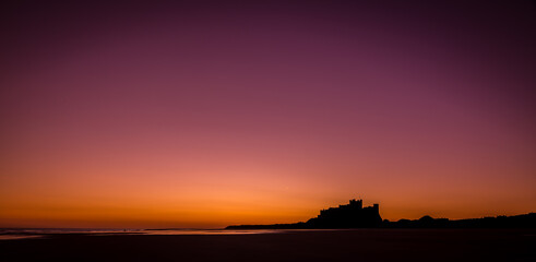 Fototapeta na wymiar The iconic Bamburgh Castle in Northumberland at sunrise, with the nearby beach deserted. 