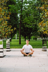 Young man wearing sportswear practicing yoga in the park. Man sit in lotus position and meditate during sunrise between mirrors.