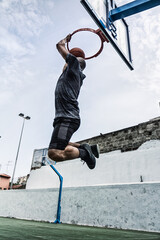 a man dunking a ball into a basketball hoop on a court in the streets in the afternoon.