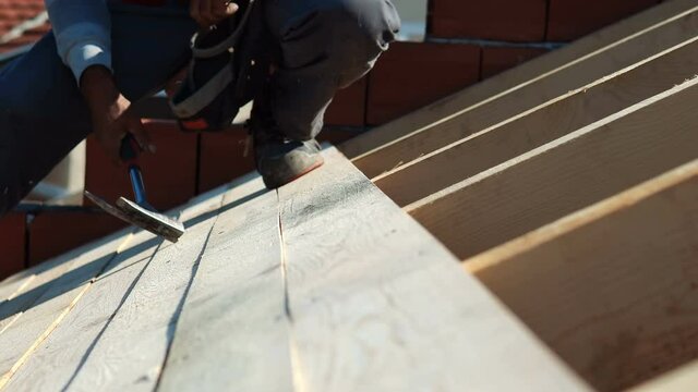 construction roofer carpenter worker nailing wood board with hammer on roof installation work