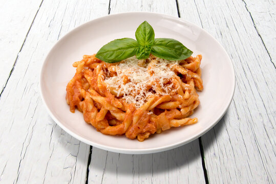 Strozzapreti macaroni pasta with tomato sauce, basil leaves and grated parmesan in white plate on white wooden table