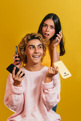 Vertical shot of Two caucasian models posing with smartphones in front of a yellow wall