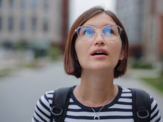 Close up face of beautiful Hispanic or Asian woman in glasses with brown hair outdoors. Confident stylish lady outdoor with copy space, emotional portrait of a tourist in the city