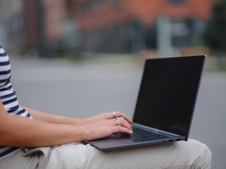 Young asian female student working at laptop sit down on bench outside on urban city street. Happy lady distance learning, education and online shopping. hands closeup