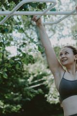 Vertical shot of woman doing monkey bar exercises in the park. Concept: outdoor active lifestyle