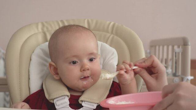 Portrait of a newborn who is spoon-fed cottage cheese. Spoon-feeding your baby with yogurt