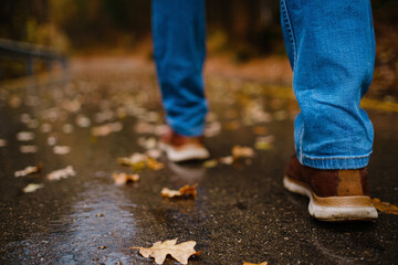 feet of a woman walking along asphalt road in autumn forest in the rain. Pair of shoe on slippery...