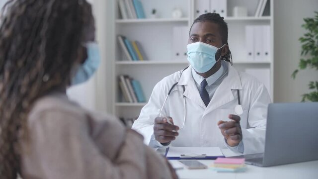 Black doctor in medical mask consulting pregnant woman, prenatal care, covid-19