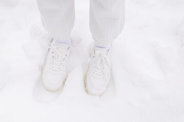 Woman in white pants and white sneakers stands in a snow.