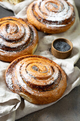 Sweet spiral bun with poppy seeds and powdered sugar large on a dark background. Delicious yeast pastries close-up. The concept of homemade high-calorie pastries