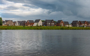 Naklejka na ściany i meble Modern dutch houses along water in Teteringen city district, on a stormy afternoon