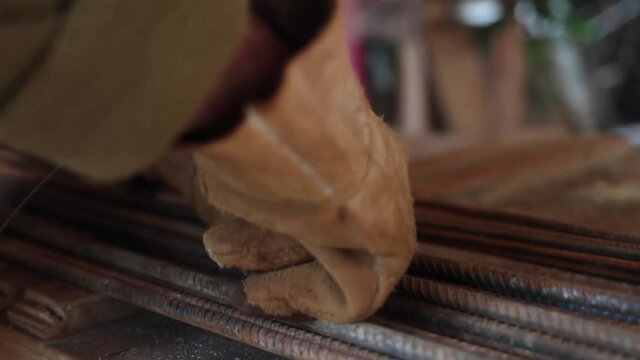 Closeup of construction worker gathering rebars with a wire, and using gloves at construction site 