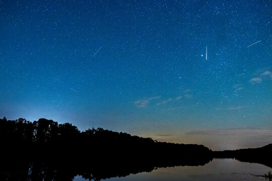 Deszcz meteoryt&oacute;w podczas maksimum Perseid&oacute;w. R&oacute;j spadających gwiazd w nocy. Najbardziej spektakularne meteory nad jeziorem.