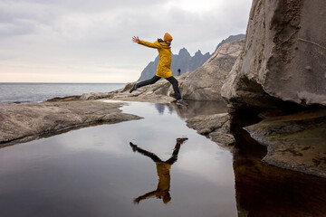 Woman, having fun in Tungeneset, Senja, Norway, jumping over big puddle, making reflection in water