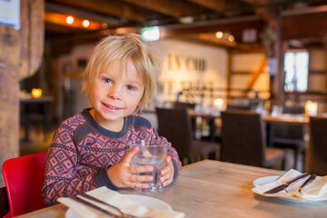 Fototapeta na wymiar Preschool child, cute boy, drinking water in a restaurant, cozy atmosphere, local small restaurant in Tromso, Norway