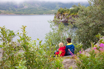 Naklejka na ściany i meble Beautiful children, cute boys, sitting on a rock on the edge of a fjord in Lofoten