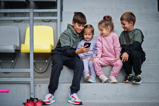 Four cuttie kids sitting on sport area and looking at mobile phone.
