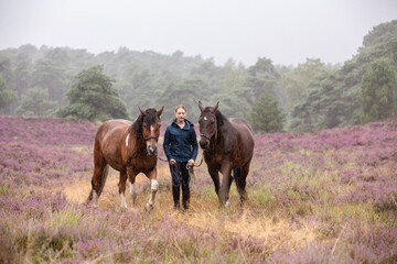 Reiterin wandert mit Pferd durch die Heide im Regen