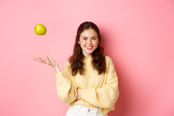Young smiling woman looking with confidence, throwing apple in air, eating healthy fruits to keep...