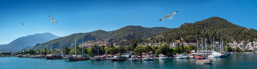 Fototapeta na wymiar Panoramic landscape of the seaport of Fethiye, Turkey. Fethiye harbour with luxury sailboats and yachts on the Aegean coast.