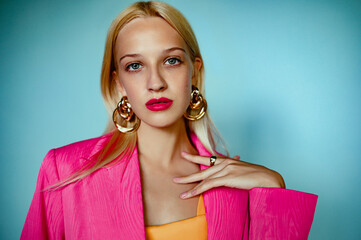 Beautiful fashionable blonde woman with blue eyes, pink fuchsia color lips makeup, wearing big trendy circle earrings, stylish summer blazer, posing on blue background. Copy, empty space for text