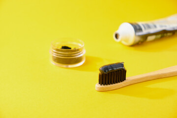 bamboo toothbrush with black charcoal toothpaste with coal yellow background