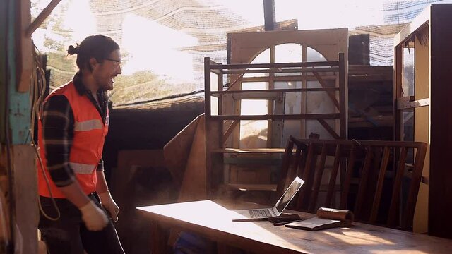 Young and handsome caucasian carpenter in the carpentry shop is Shouted with joy Hop and dance until the dust spreads. Because the customer confirms the order for wooden furniture products via email.