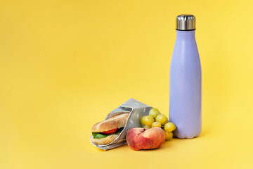 Reusable bottle and sandwich wrap on bright yellow background. Lunch at work, healthy snack at school concept