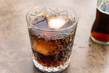 Crystal glass with bubbly and iced cola, with a bottle in the background out of focus.